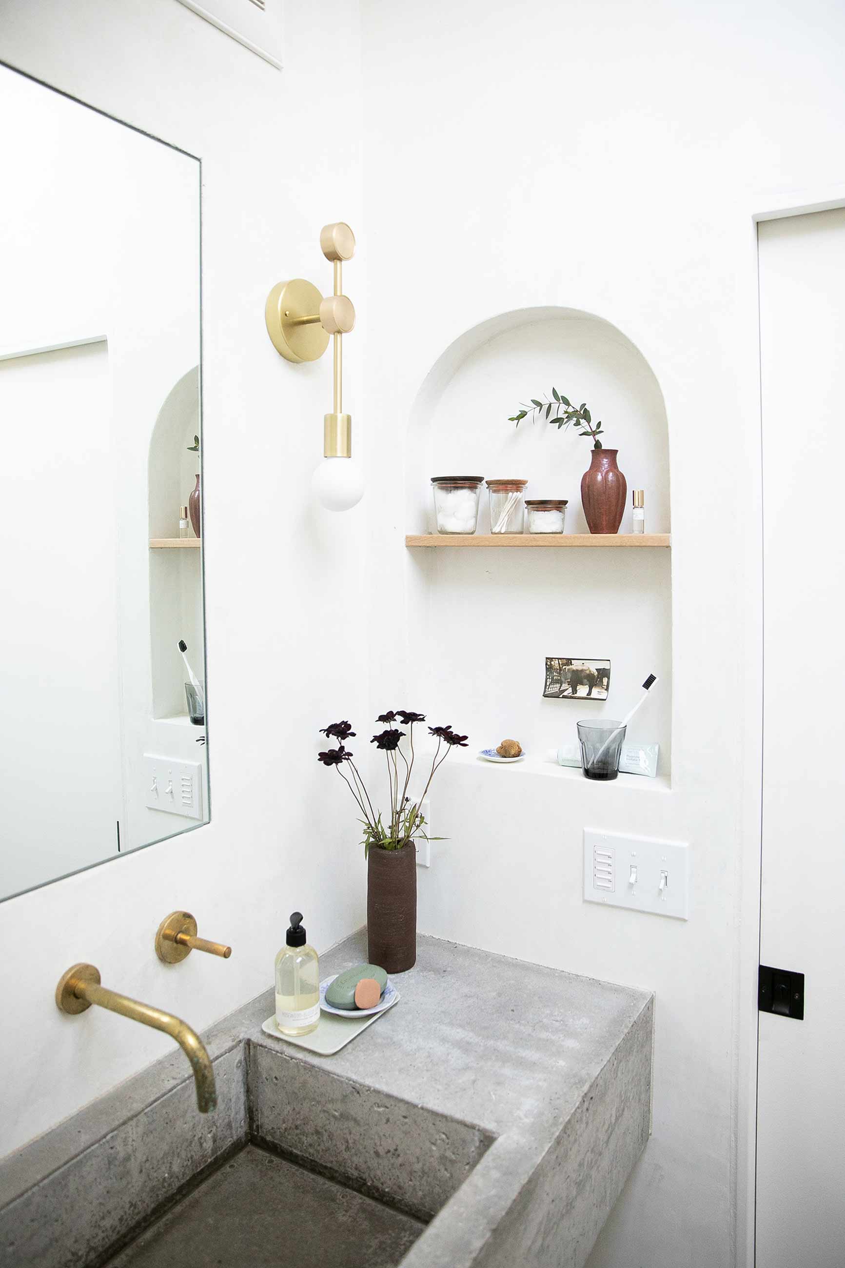 White modern bathroom with gold wall sconce and concrete sink. 
