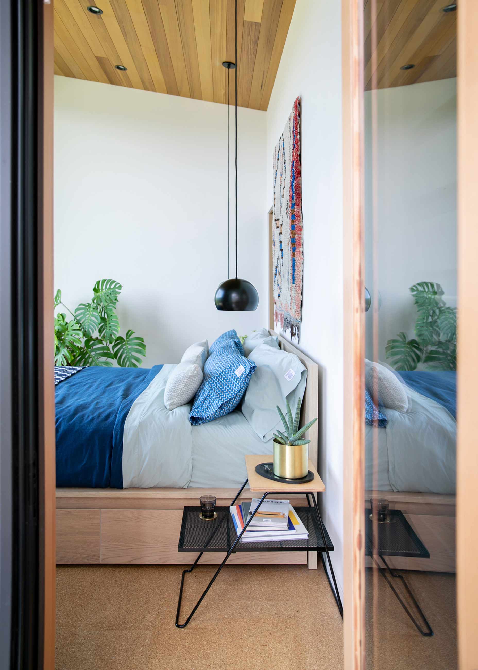 View into modern bedroom with low bed and blue bedding from doorway. 