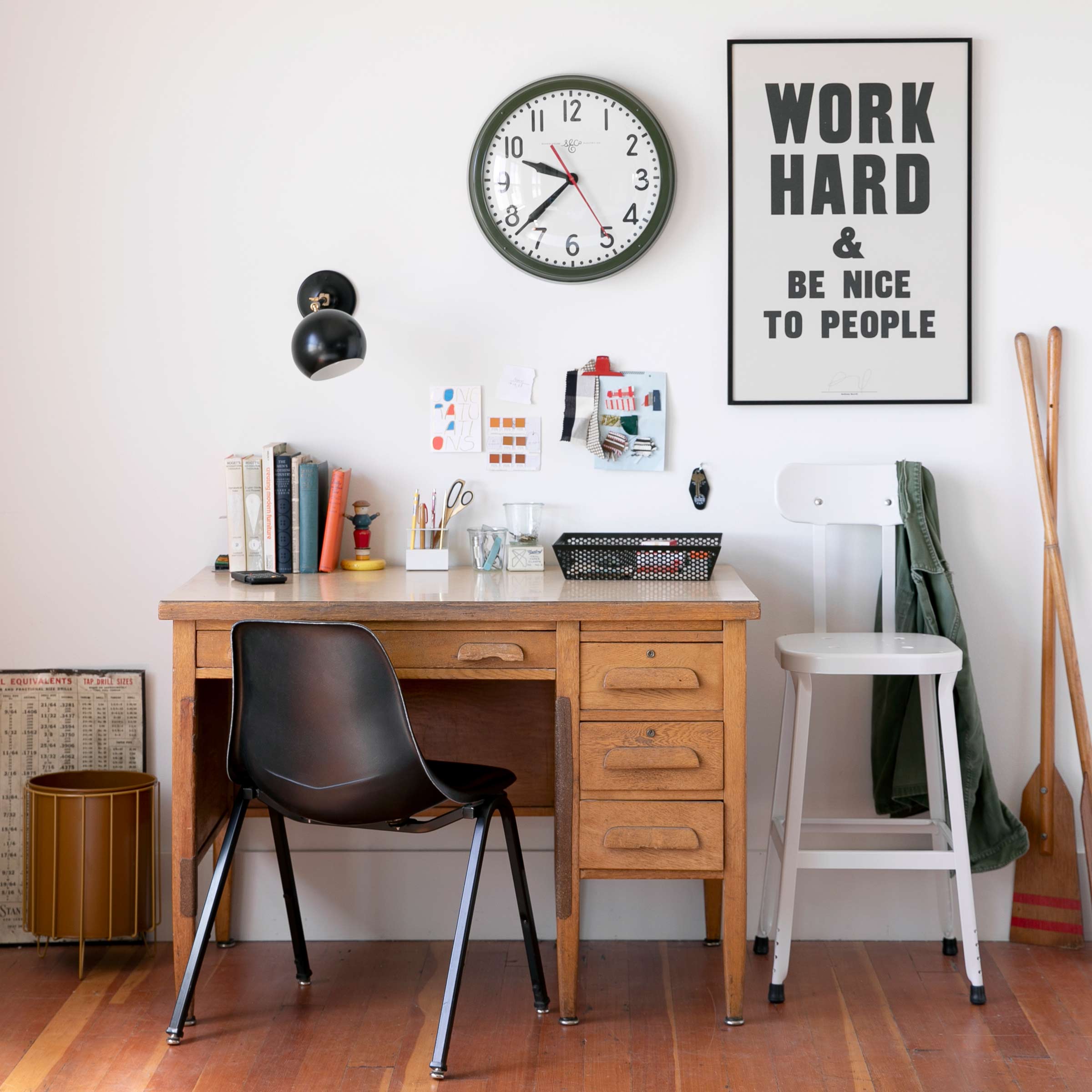 Office desk with a black wall sconce, art print, and analog wall clock. 