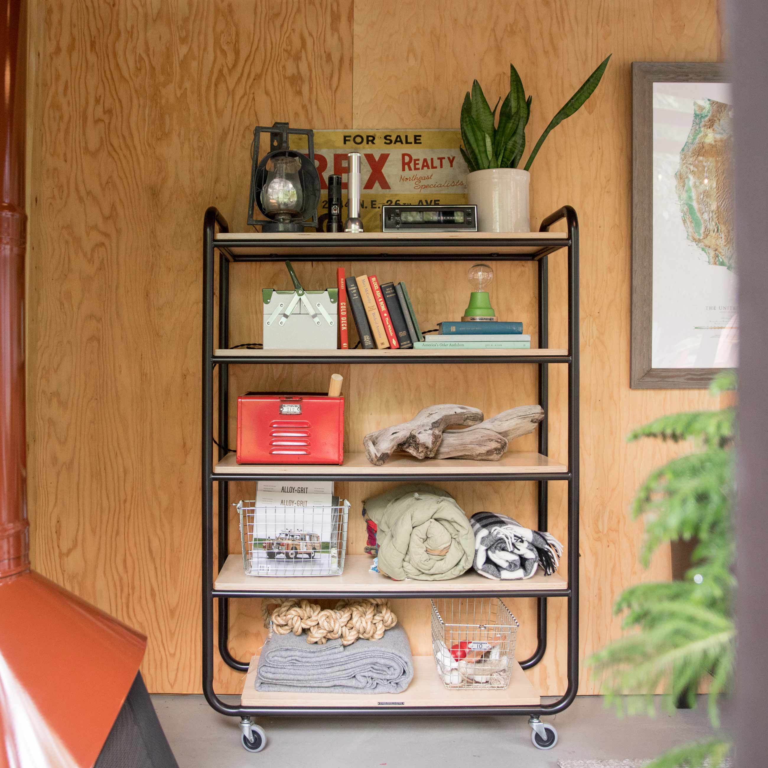 A utility cart set against a wooden wall holding a number of home decor items. 