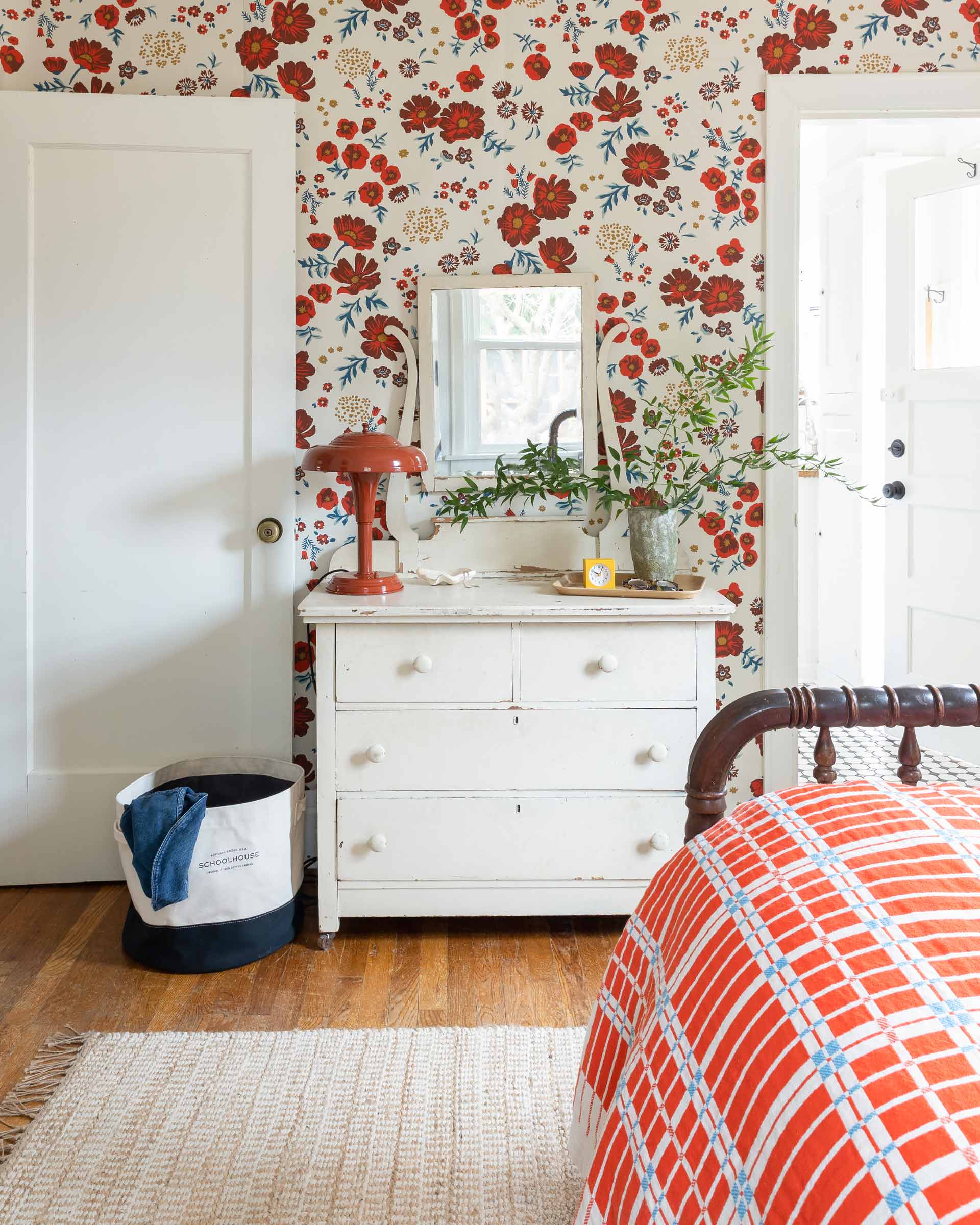 A paprika Graduate Table Lamp on a white dresser in a wallpapered bedroom. 