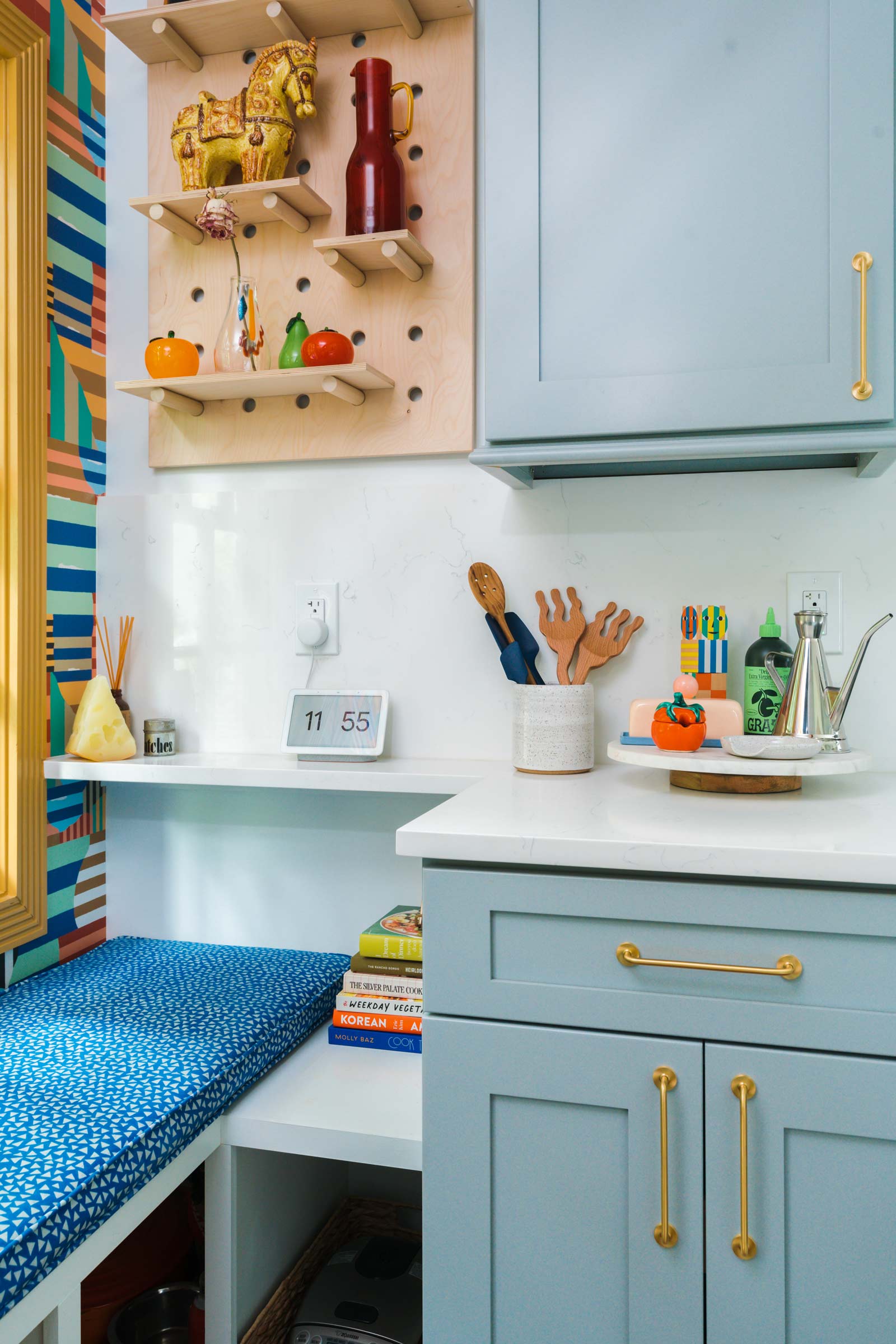 Renovated kitchen with light blue cabinets with brass pulls, a sitting bench, and a wooden pegboard on the wall. 