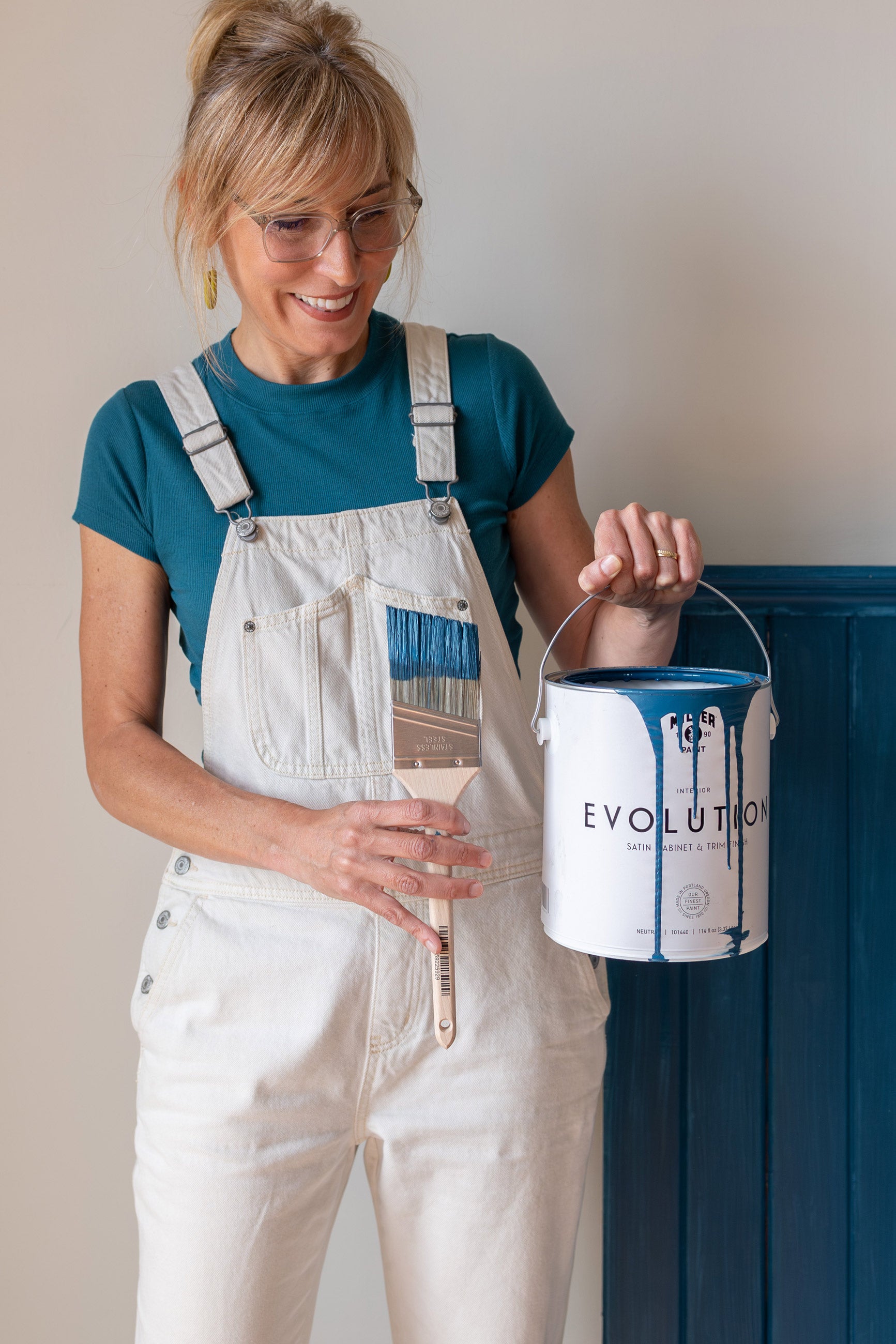 Person holding up gallon of paint and a paintbrush.