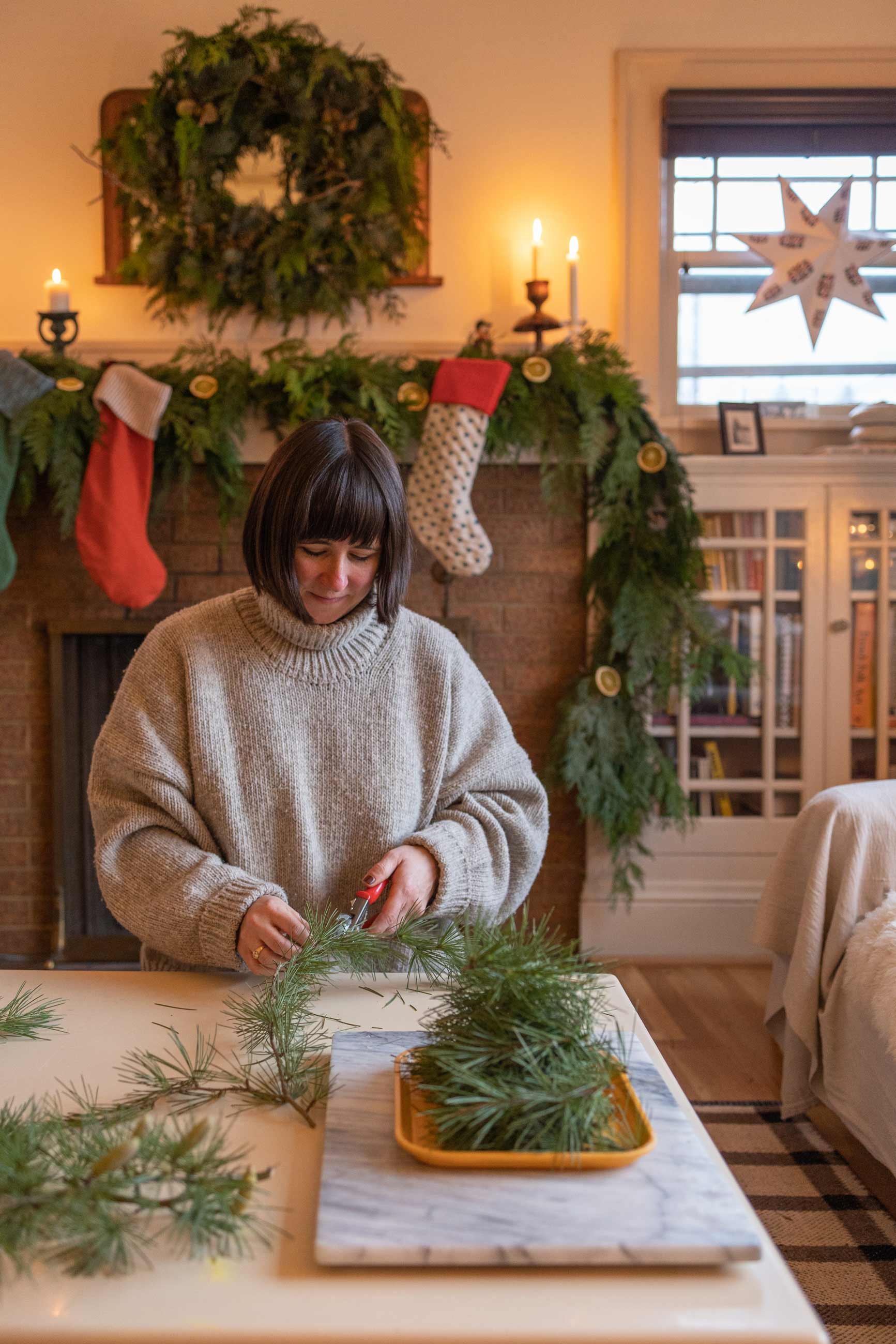Person making garland on coffee table in front of cozy fireplace.