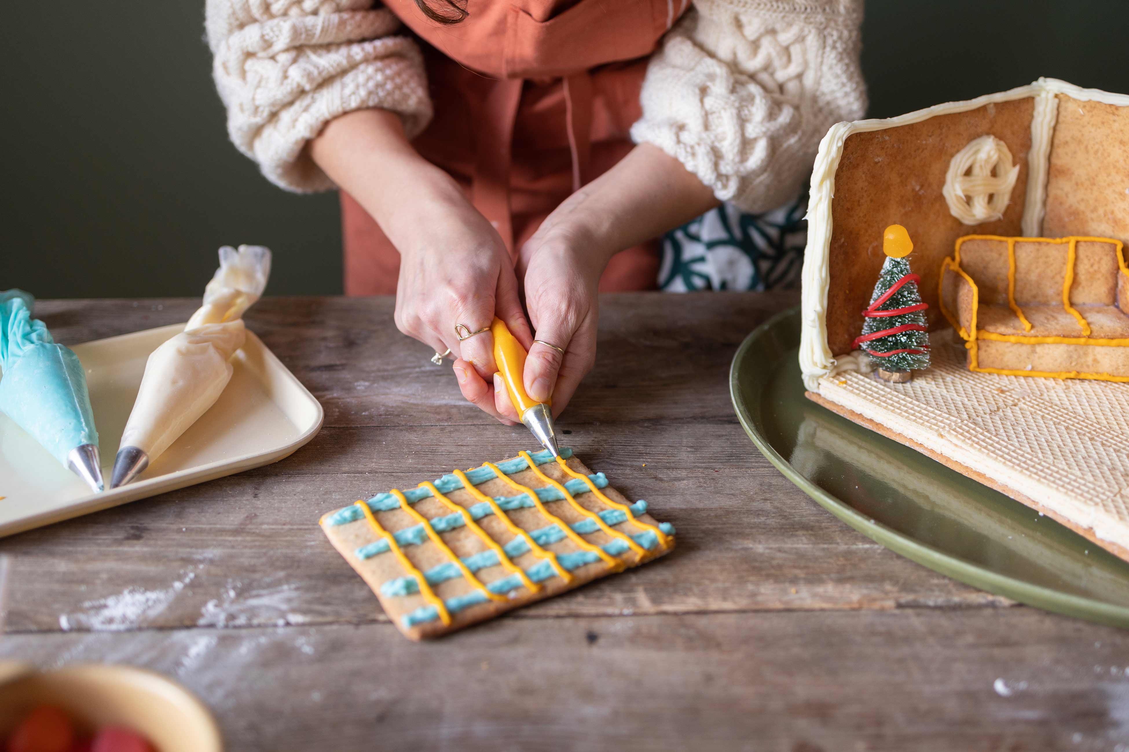 Person piping orange frosting onto piece of gingerbread in straight line.