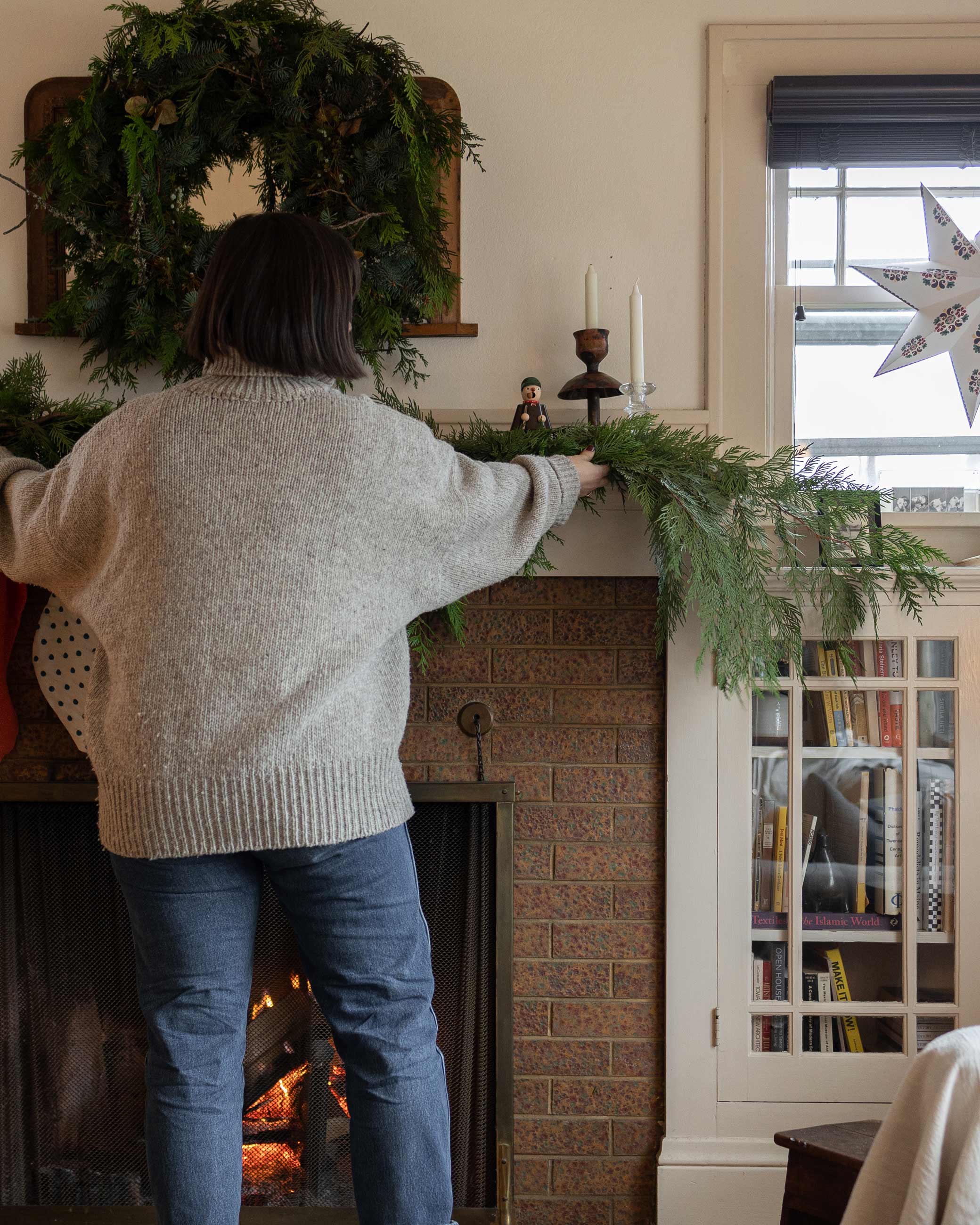 Person putting cedar garland on top of fireplace mantel.