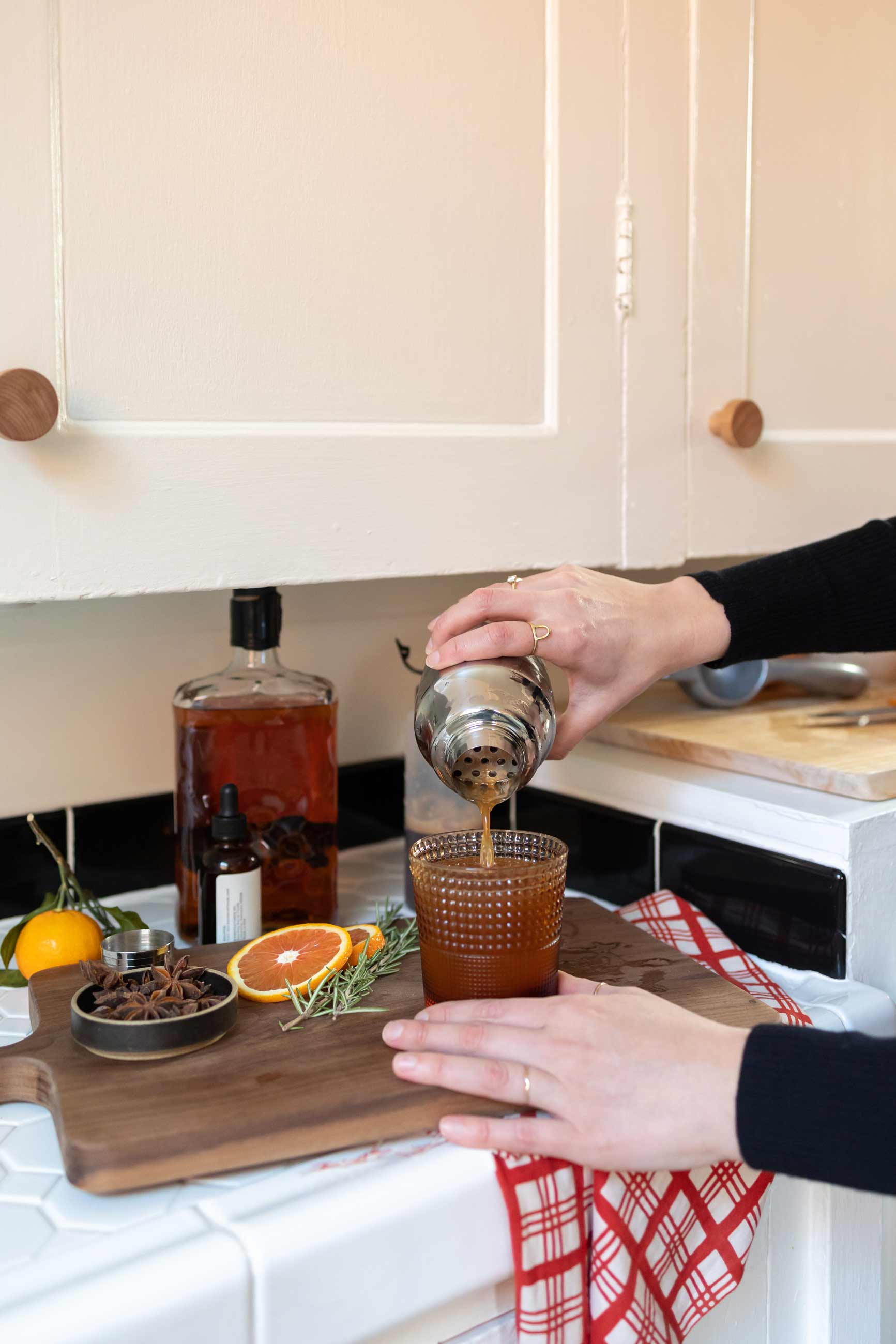 Person straining drink into amber glass tumbler on top of cutting board.