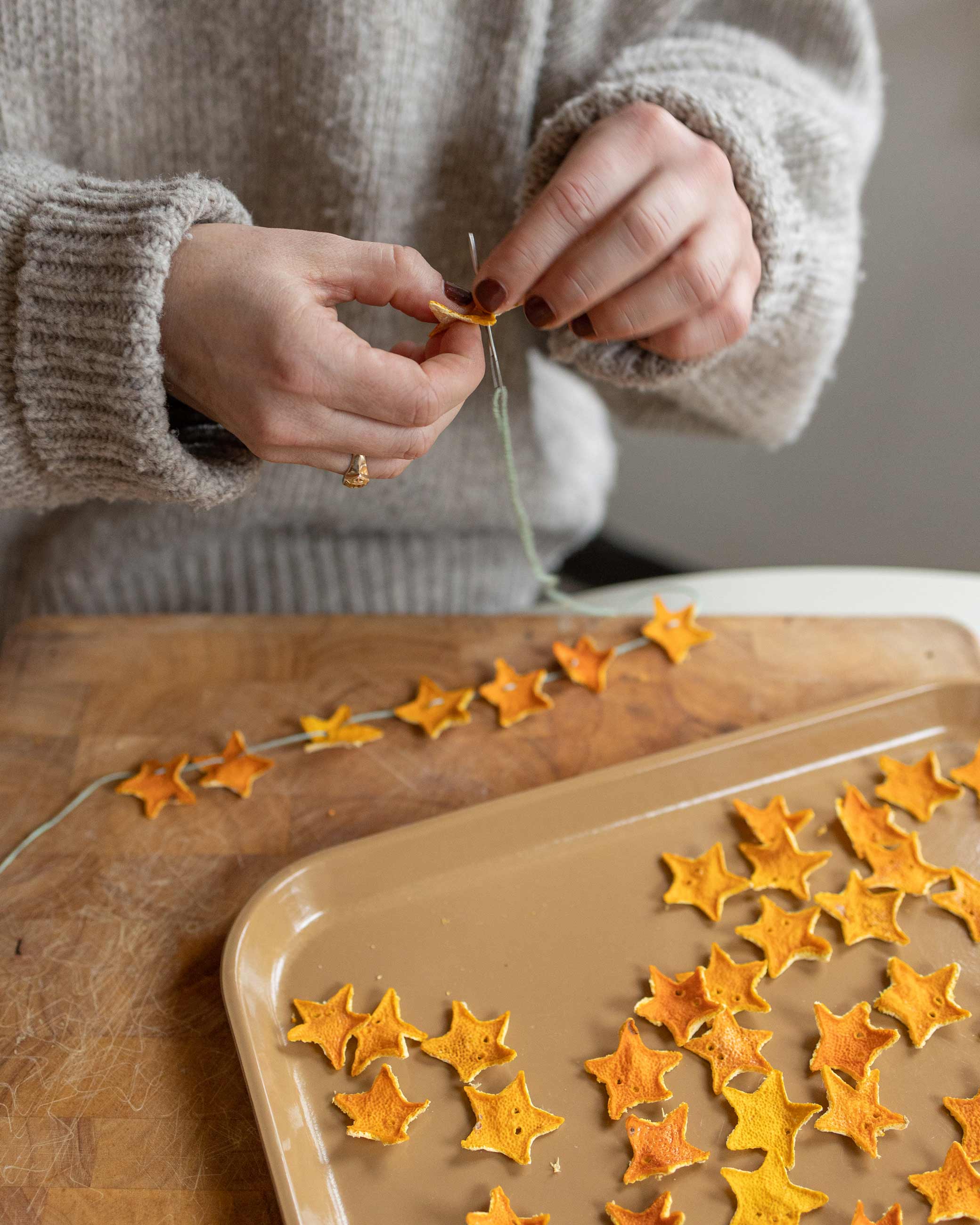 Person stringing dried stars cut out from mandarin skin together on string.