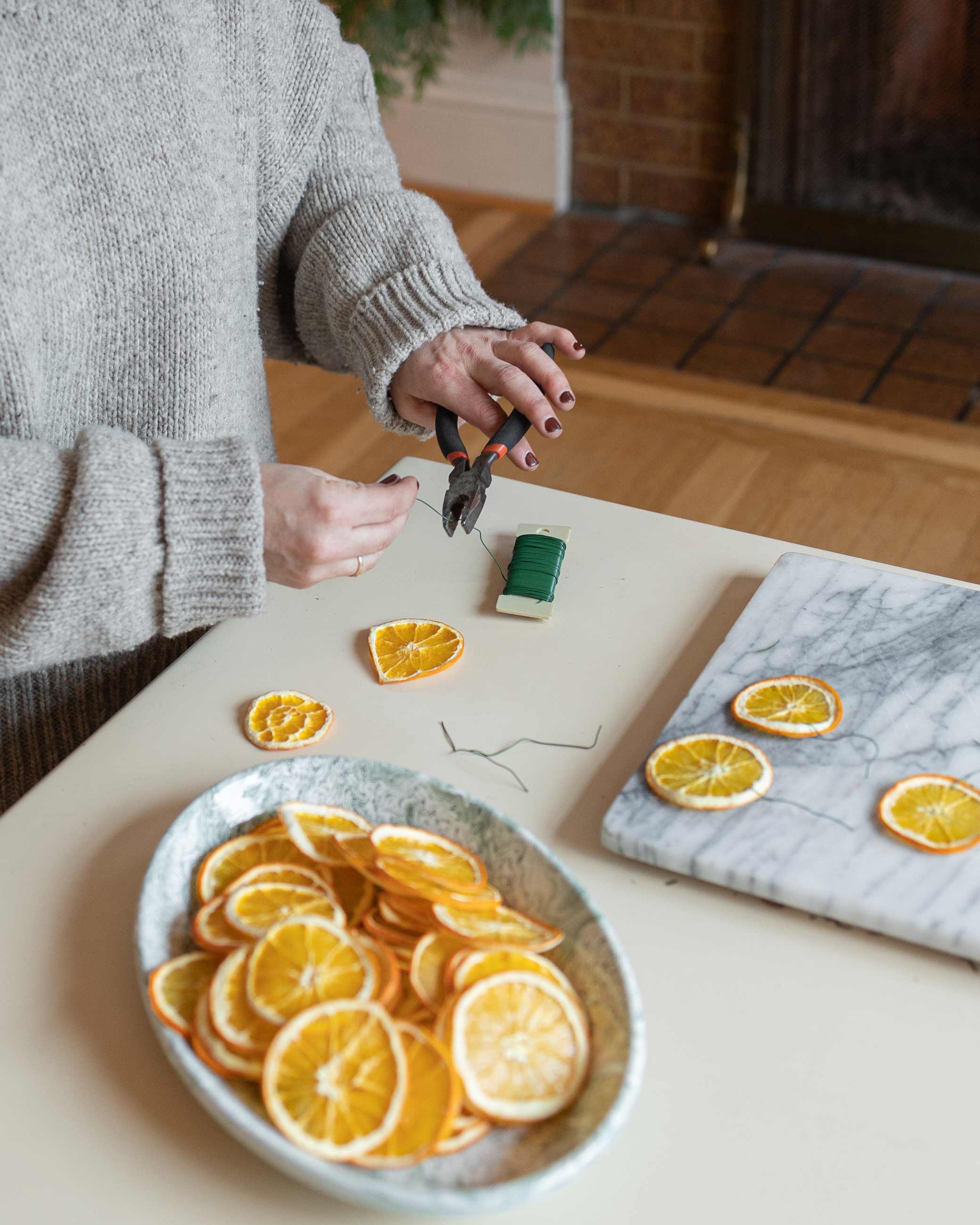 Person stringing together dried orange slices on coffee table.