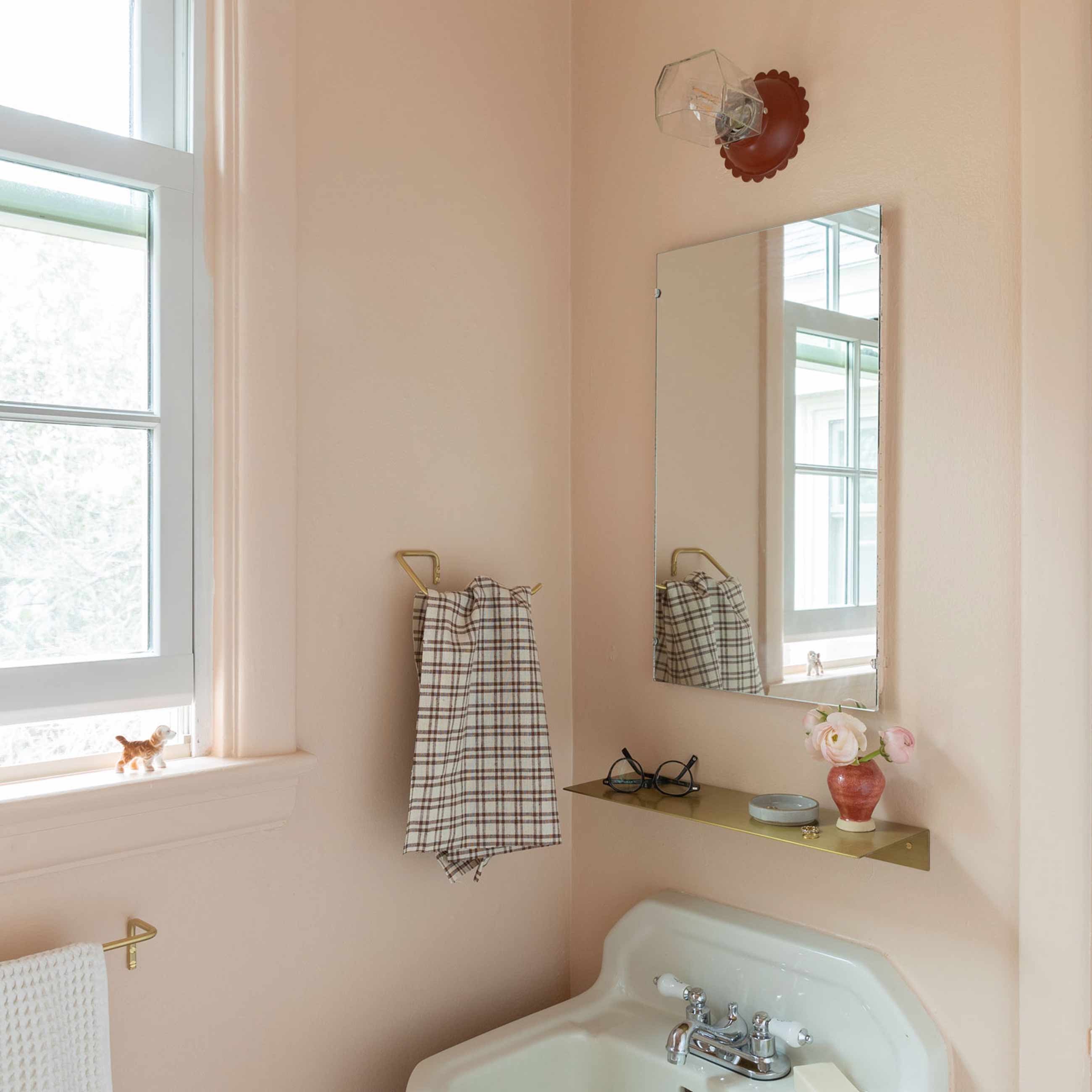 Pink bathroom with sink, mirror, small brass shelf, and scalloped light fixture.