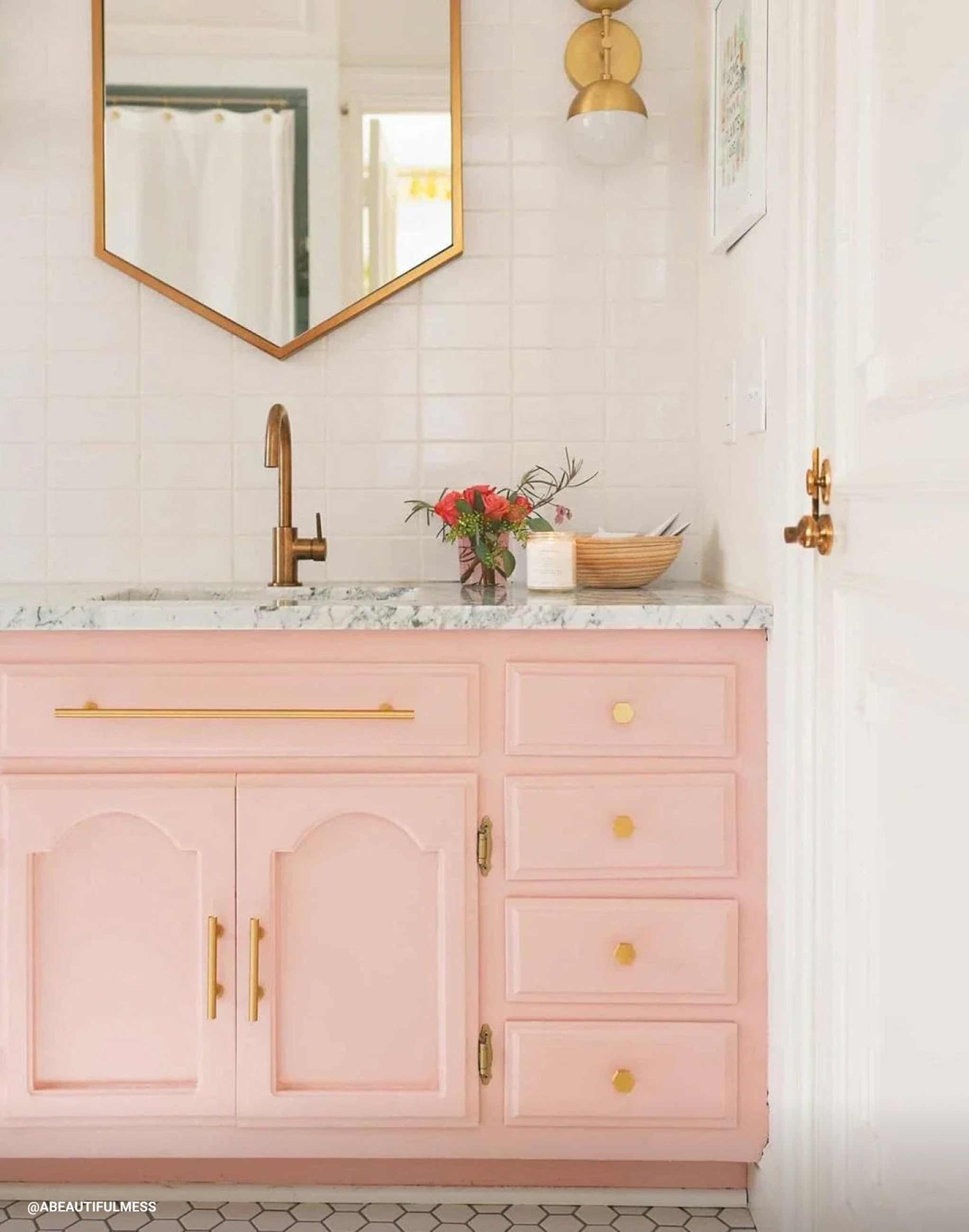 Bright pink vanity with natural brass mirror and light fixtures. 