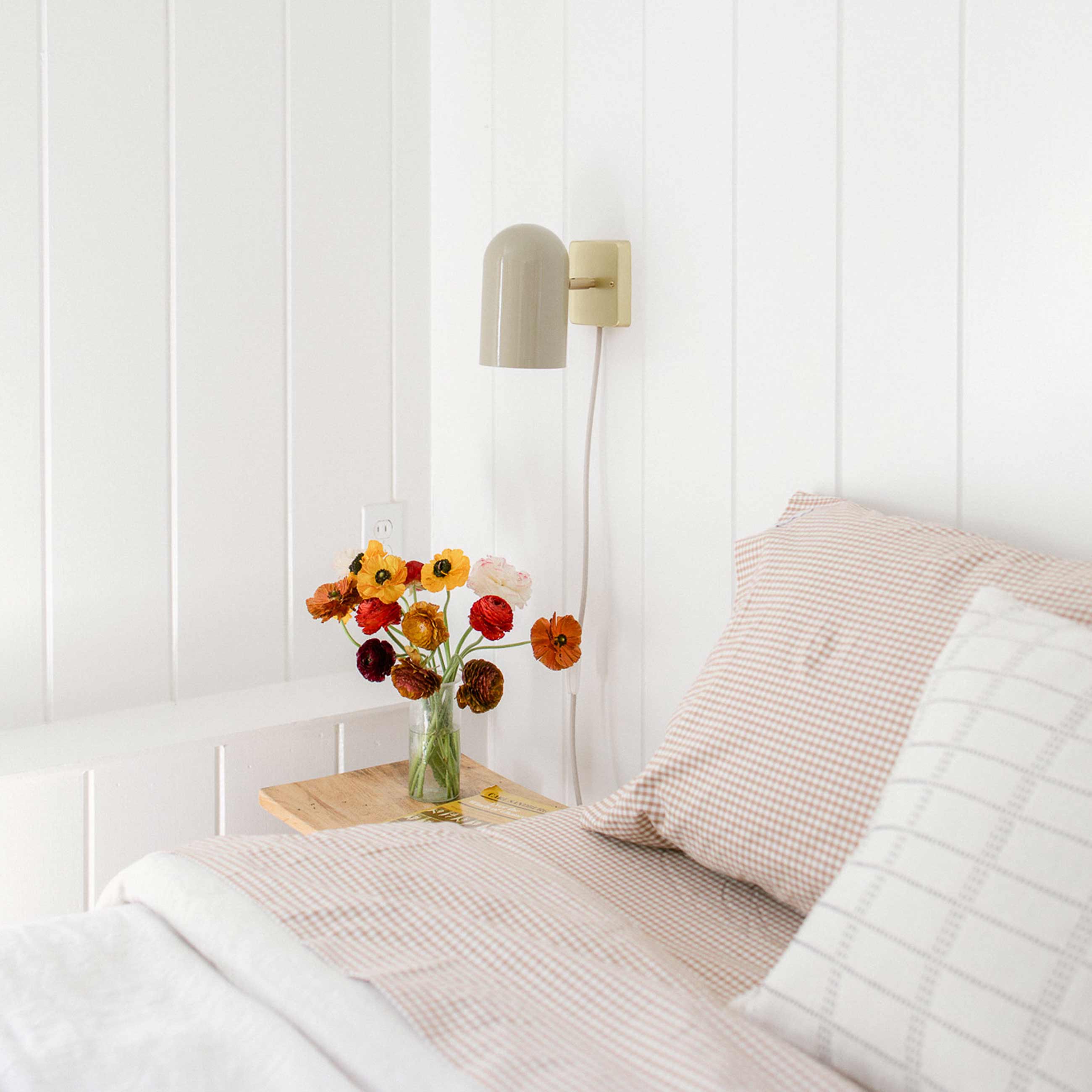 Plug-in wall sconce above nightstand next to bed in bright and airy bedroom.