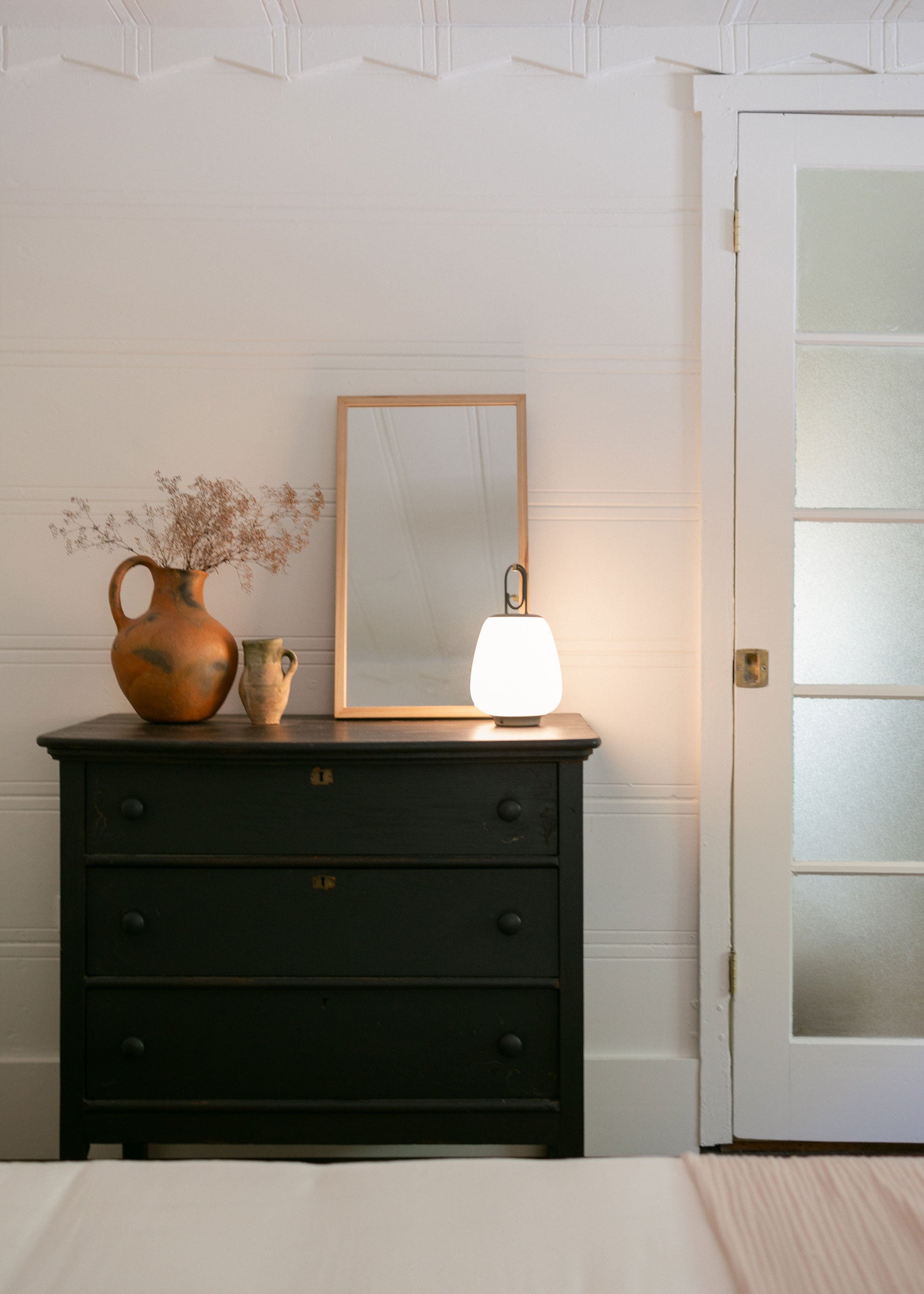 Portable lantern on black dresser with wooden mirror propped up against the wall. 