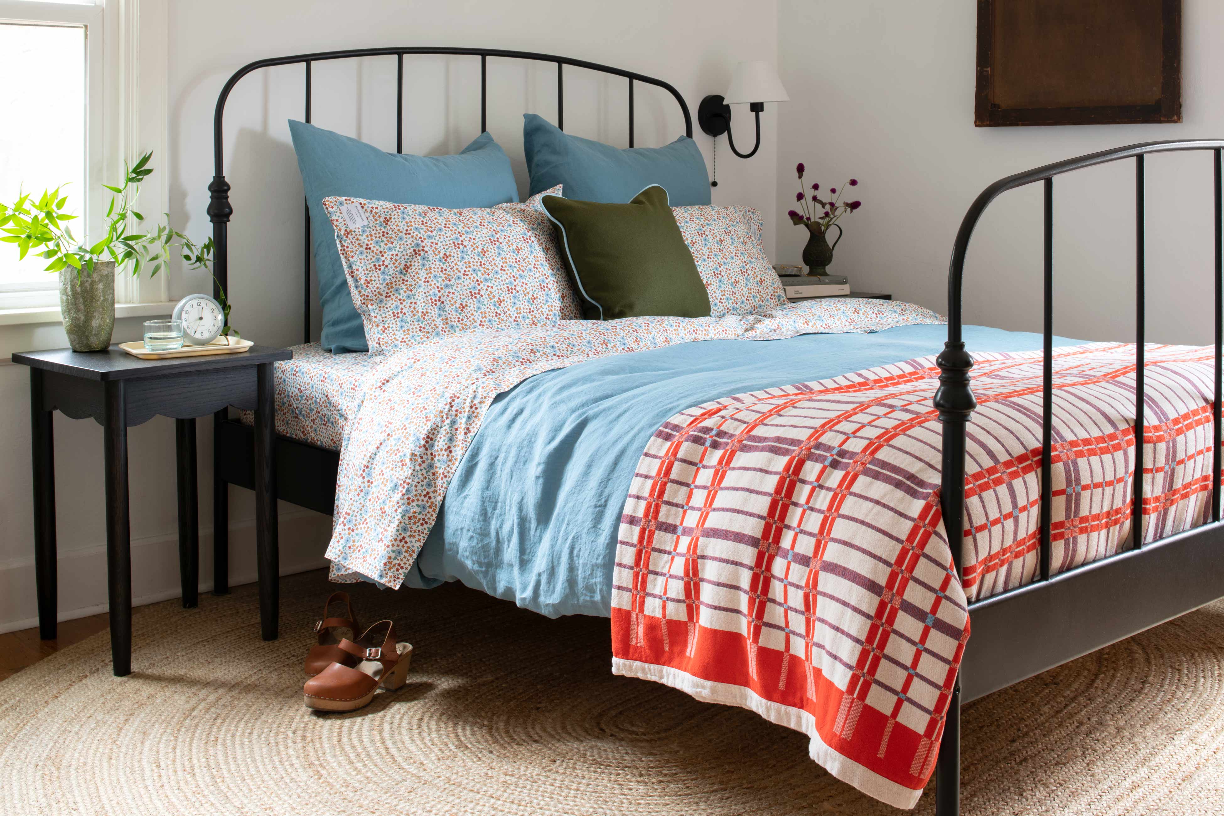 Bright and sunny bedroom with red and blue bedding on bed. 