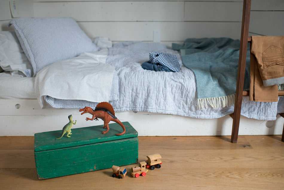 toy dinosaurs on a green chest next to a bed with a blue comforter
