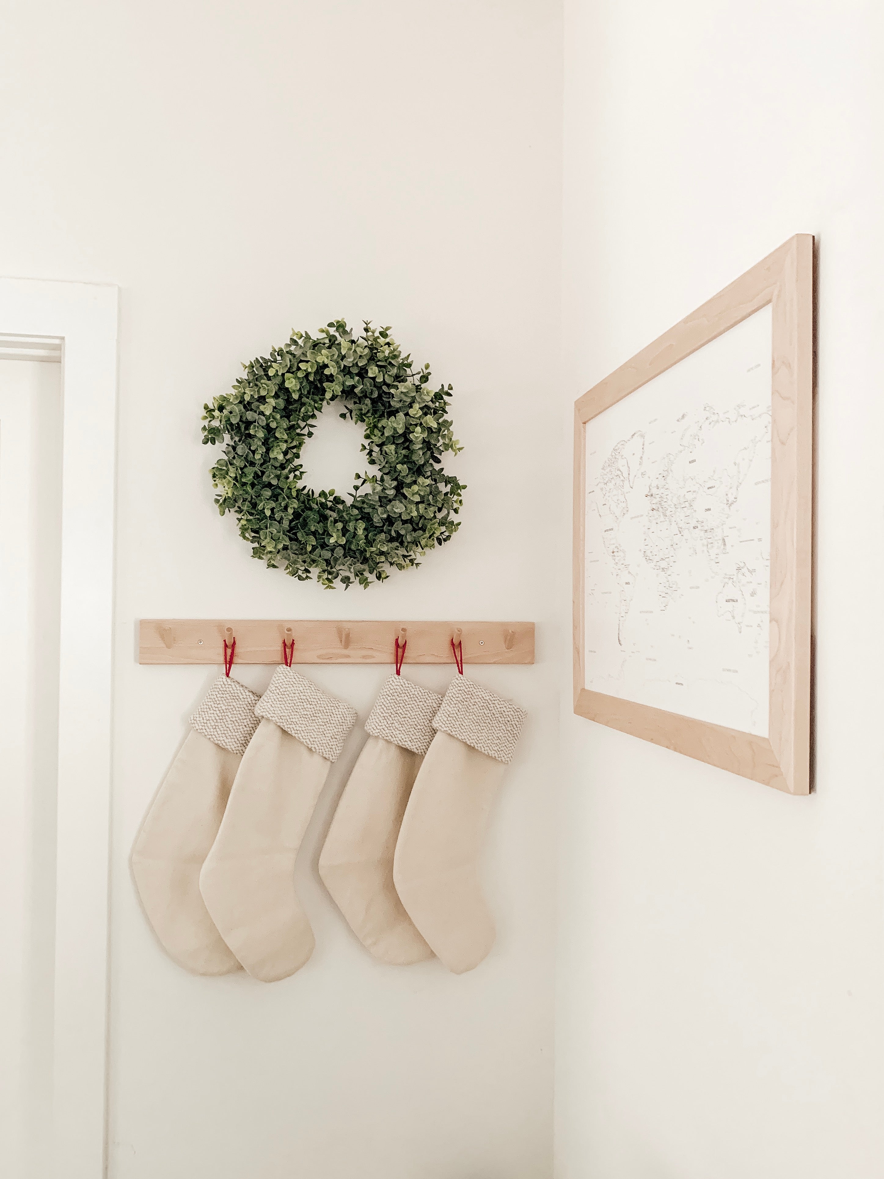 Identical white and gray stockings hanging from birch peg rail below simple holiday wreath.