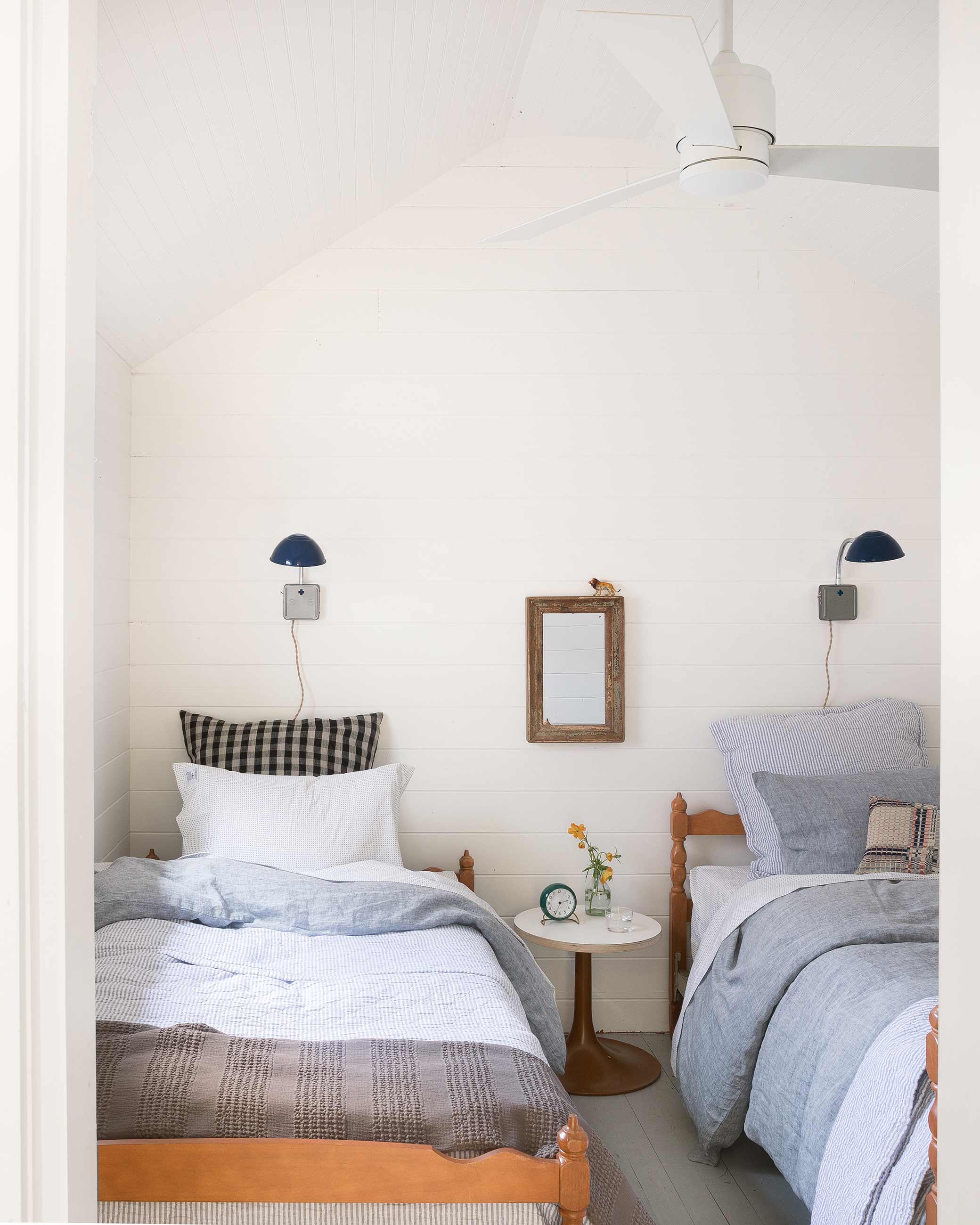 Two twin beds side by side in kids bedroom with plug-in-sconce above each one. 