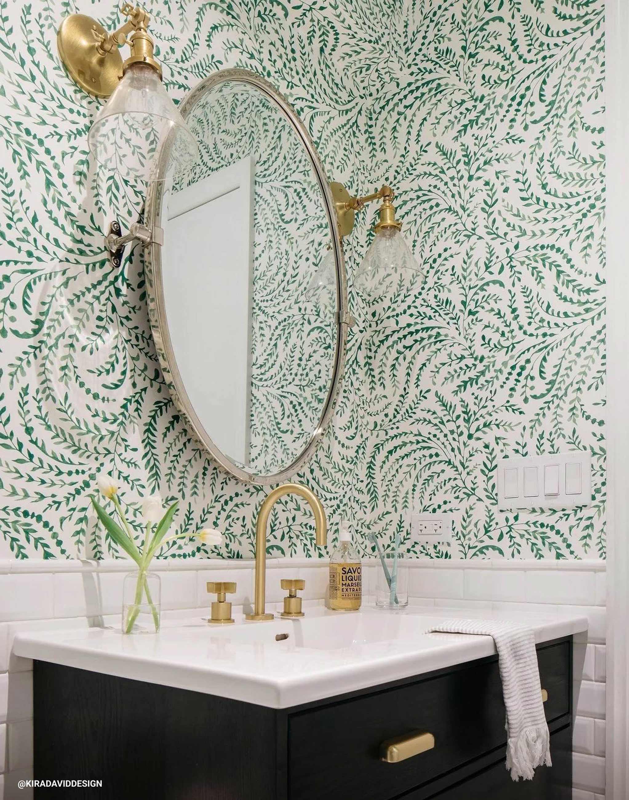Wallpapered bathroom with white vanity, sink, and natural brass light fixtures. 