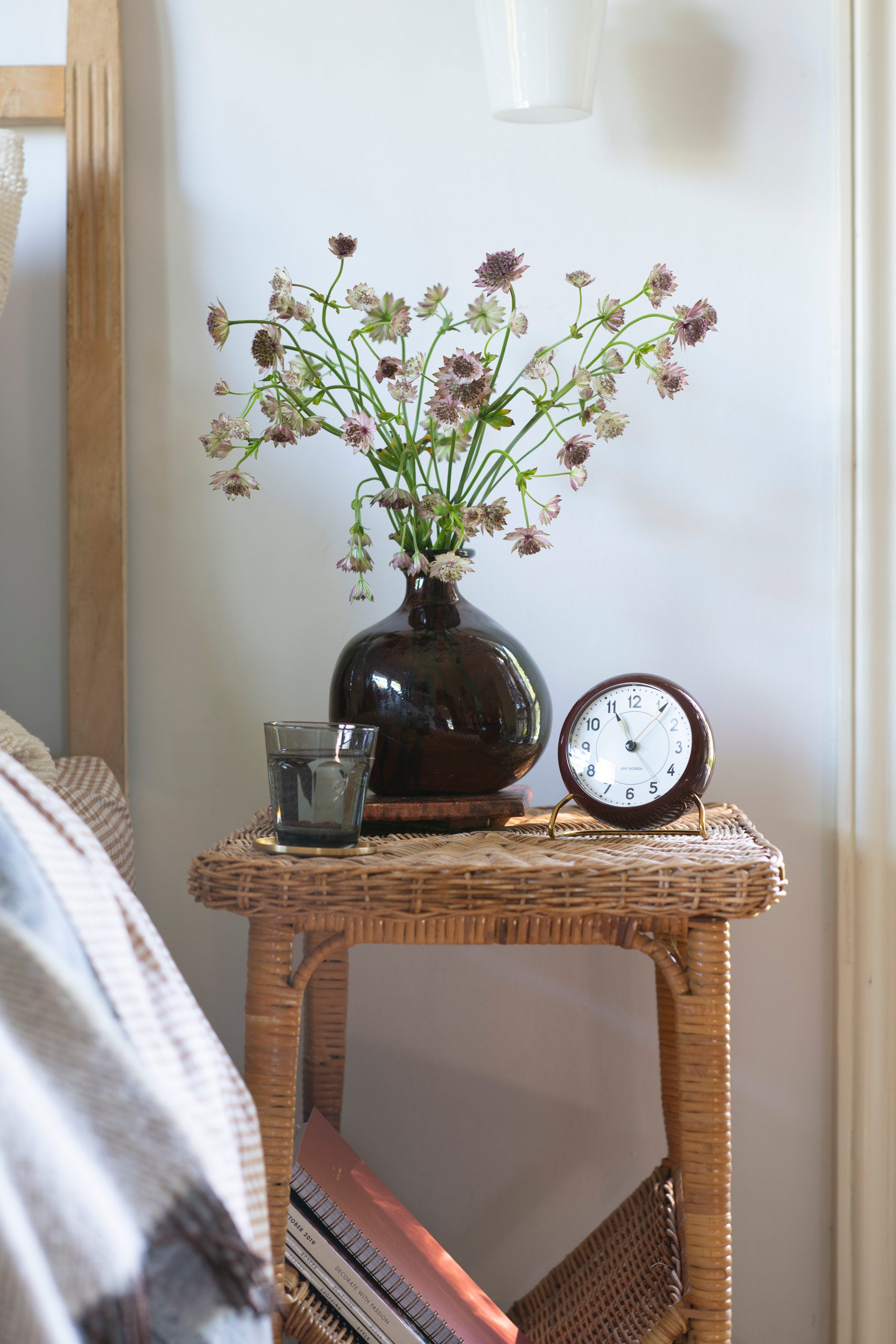 Wicker bedside table with fresh cut blooms, small clock, and water glass 