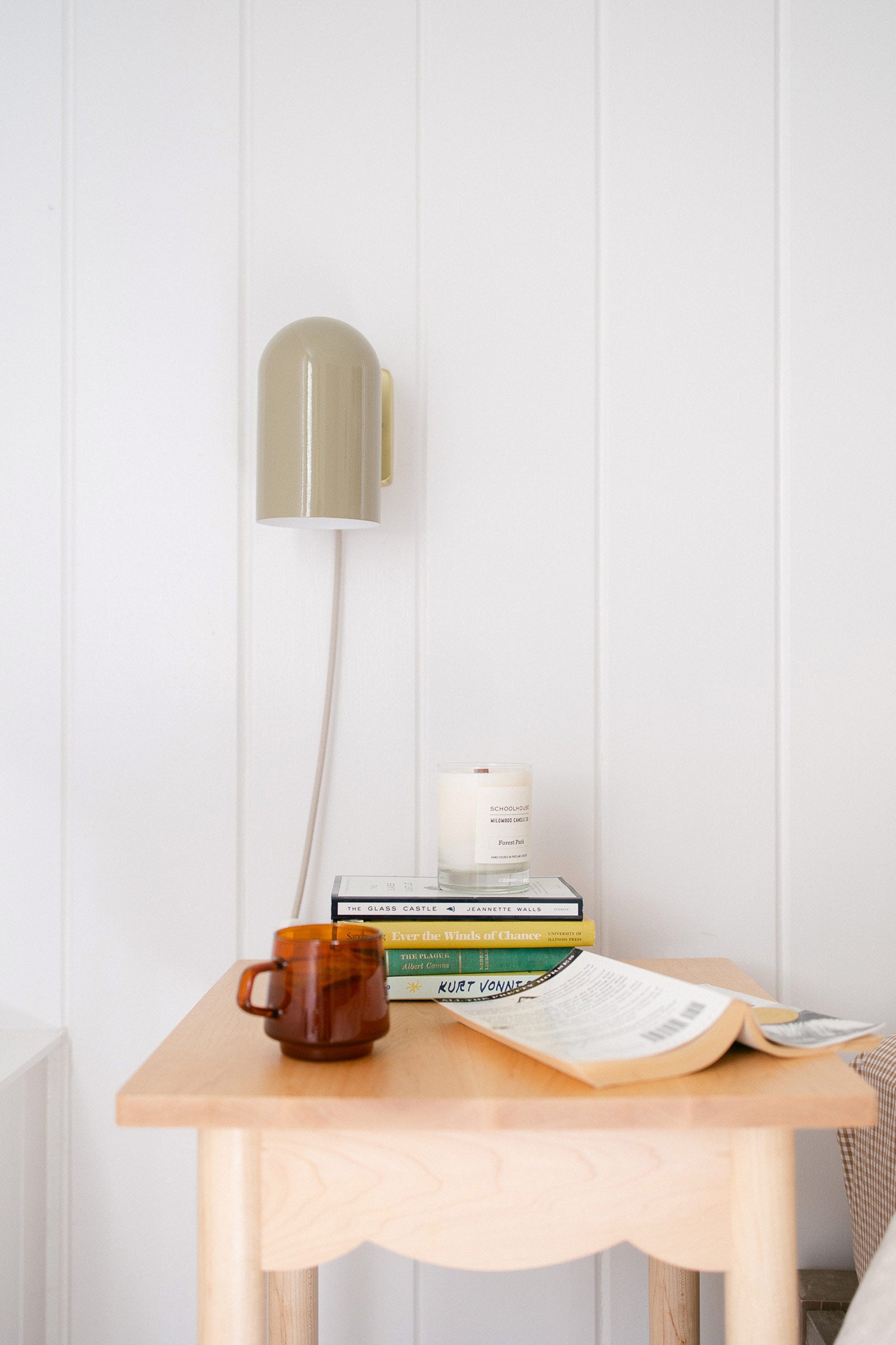 A wooden scalloped bedside table with an amber mug and stack of colorful books.