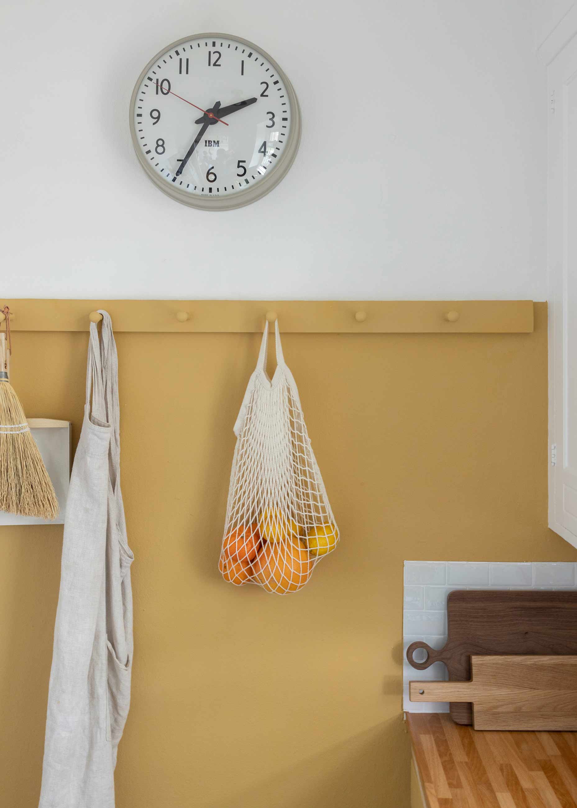 Close in shot of yellow wall with peg rail and gray clock above. 