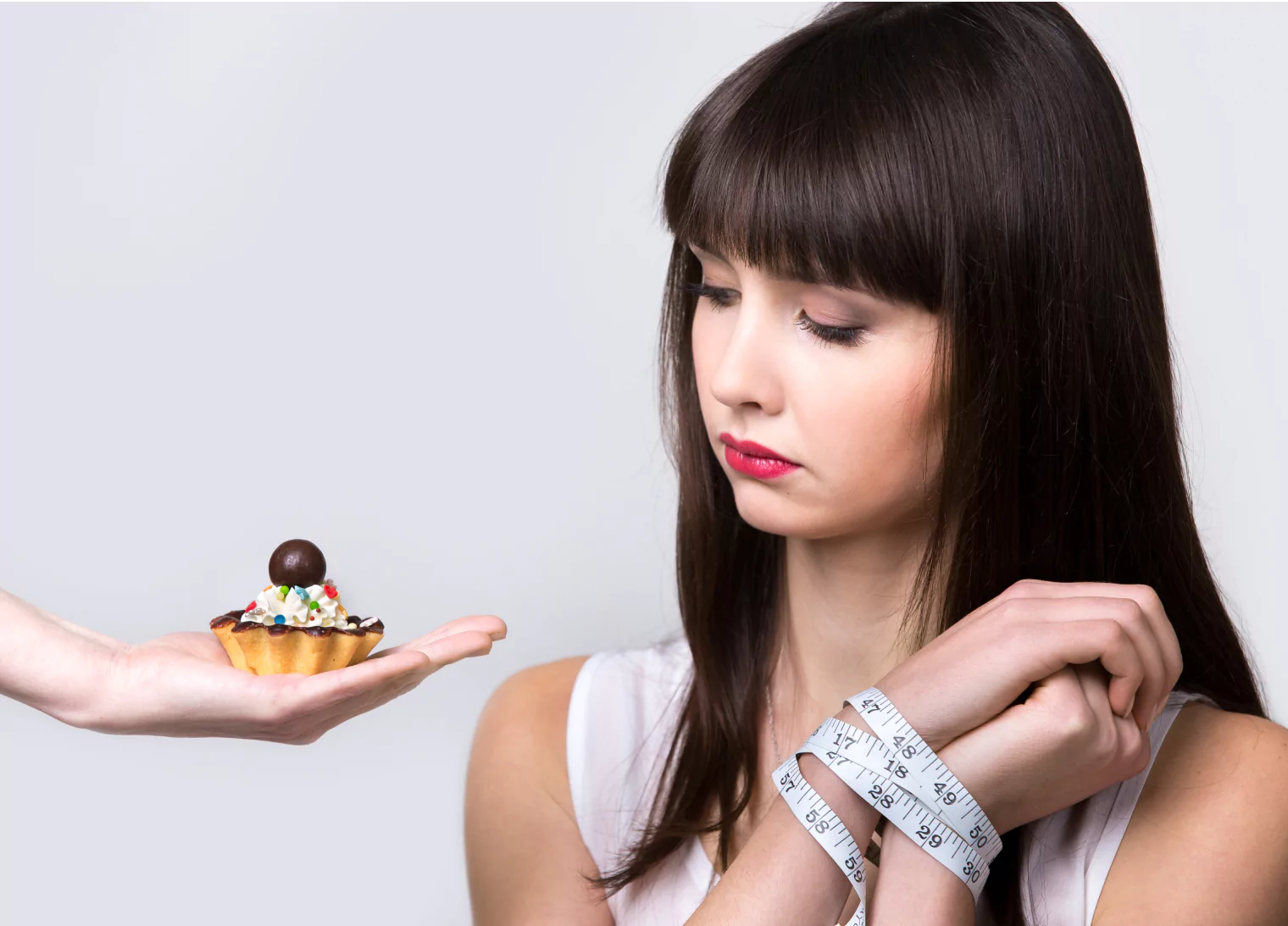 Woman looking at a cupcake, hand tied with a measuring tape.