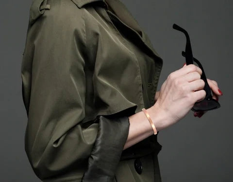 A stylish woman wearing a trench coat and glasses, with 4mm Hammered Copper Cuff Bracelet on her wrist