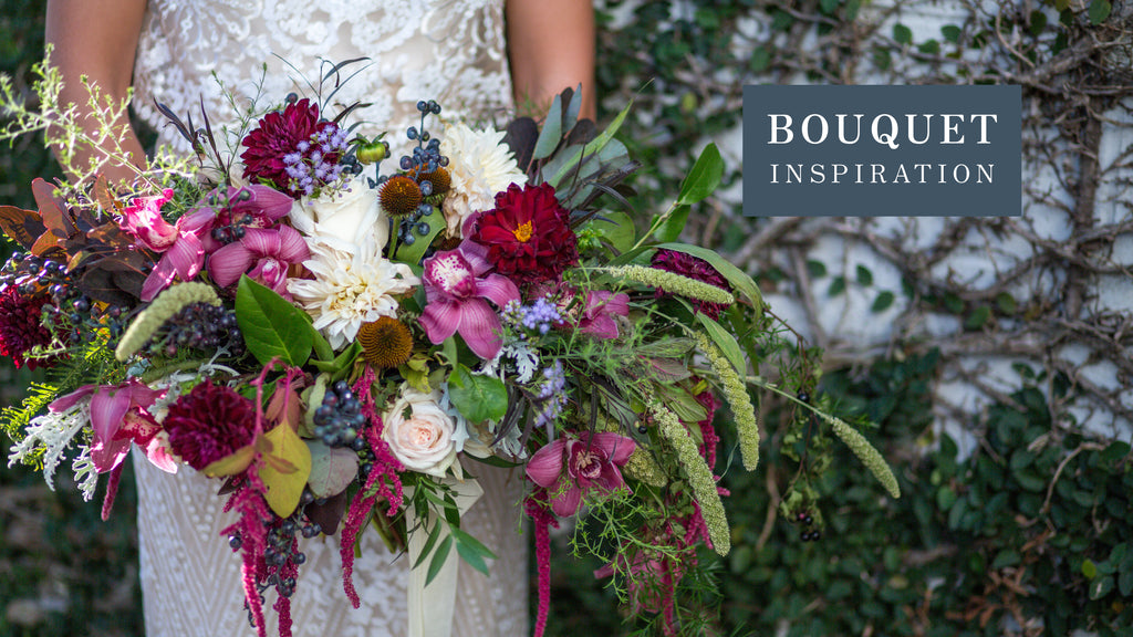 A bride holding a large, asymmetrical wedding bouquet, offering inspiration with its rich variety of flowers including deep red dahlias, pale pink orchids, white roses, and accents of purple and green foliage.
