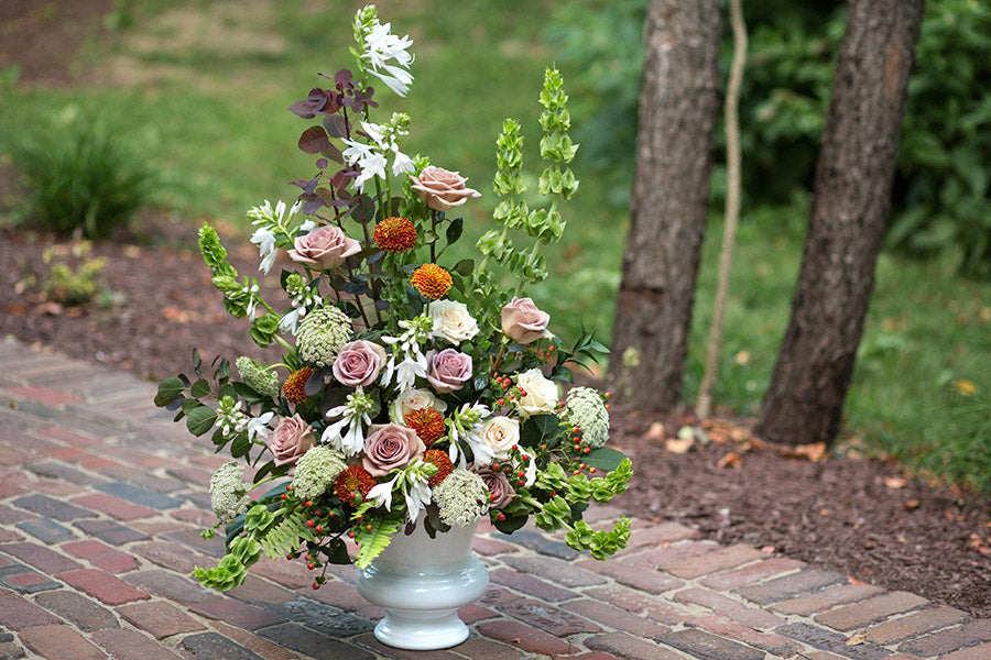 A colorful flower arrangement with Bells of Ireland in a white ceramic urn