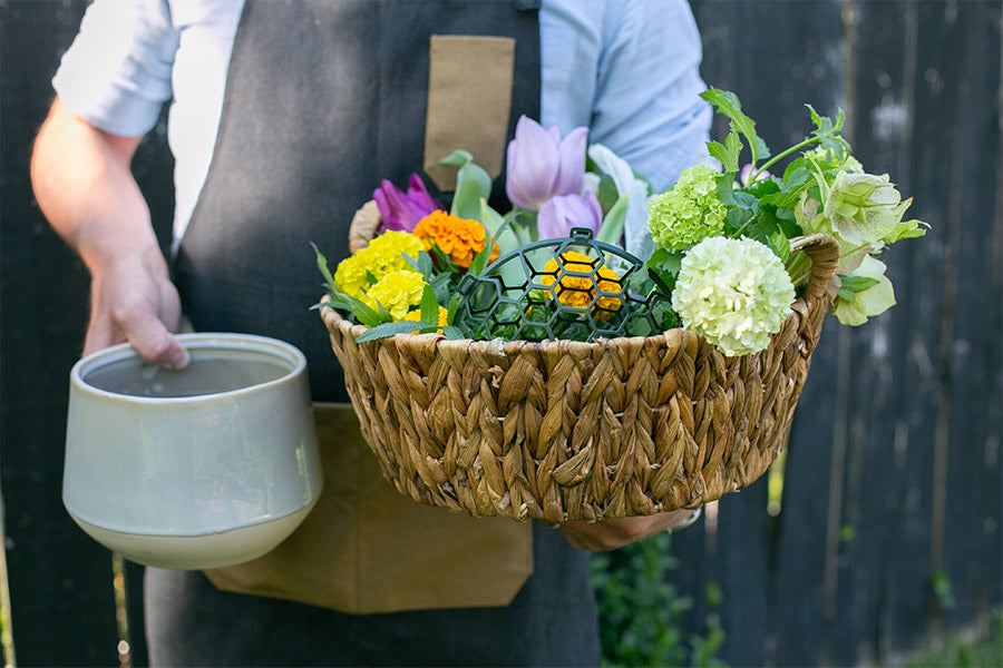 A florist holding a vase and a basket of flowers and arrangement supplies.