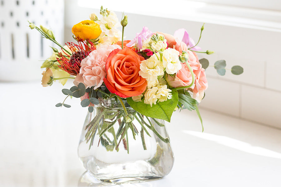 Bright orange and light pink floral arrangement in a low profile Rosie Posey clear jar
