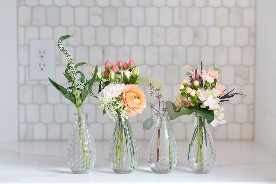 Four glass bud vases with various flowers in them