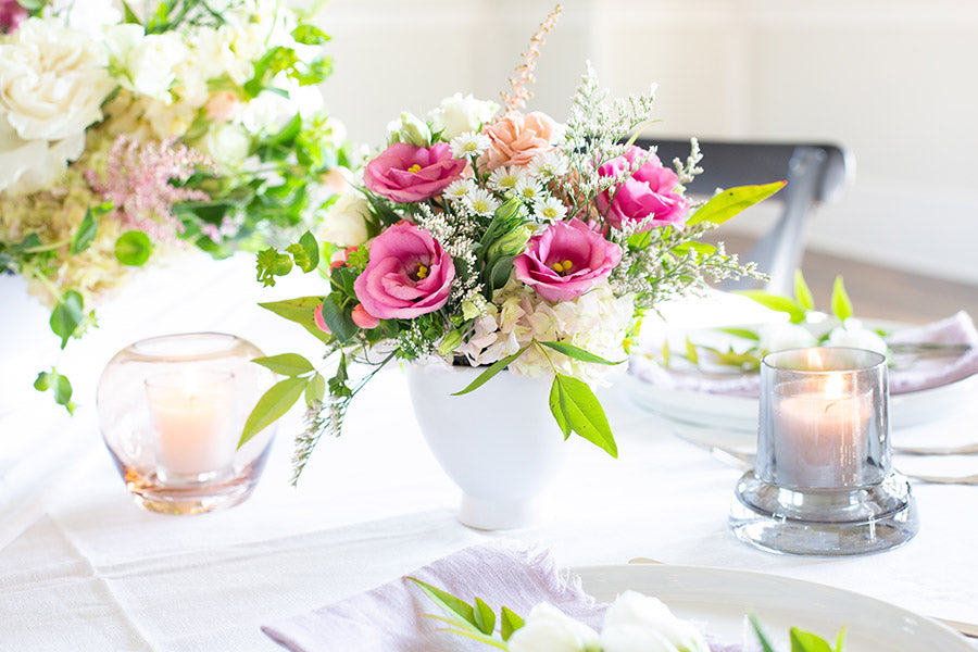 A floral centerpiece of pink flowers in a white vase on a table