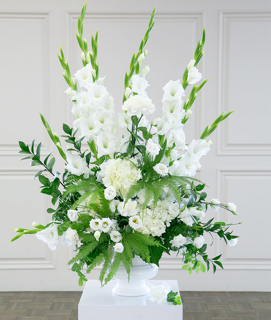 A white bowl style vase with a tall white and green floral arrangement