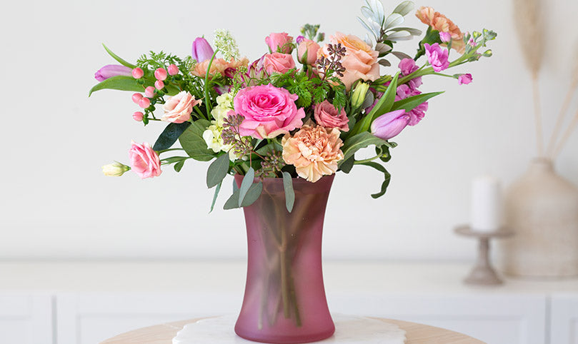  A bouquet of magenta and purple flowers in a magenta glass vase