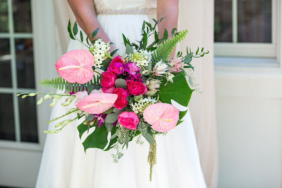 A wedding bouquet with bright pink flowers and tropical leaves arranged by a wedding florist.