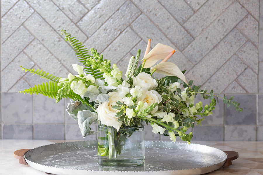 Green ferns in a white and green floral arrangement in a square glass vase.