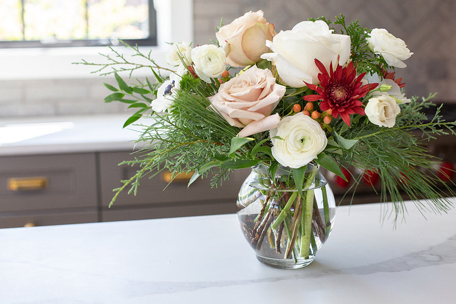 A clear bubble vase with red and white flowers and soft greenery