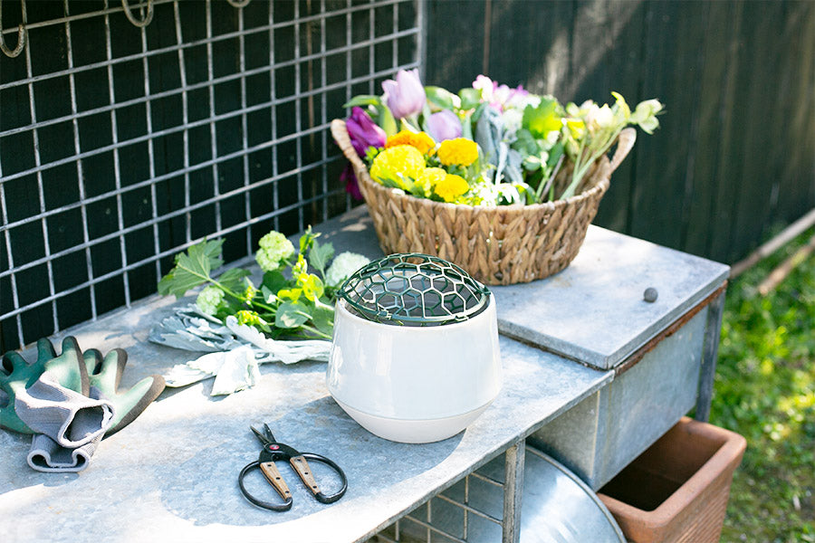 A basket of flowers, a Holly Chapple Pillow mechanic on a vase, garden gloves, and florist clippers on a workbench