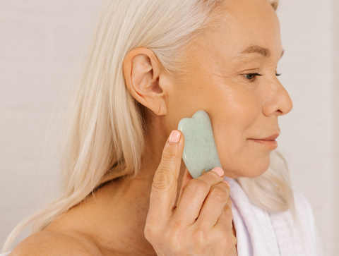 Woman applying serum to face with gua sha tool