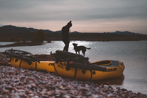 silhouette of girl and dog in river with pack rafts and bikes on boat