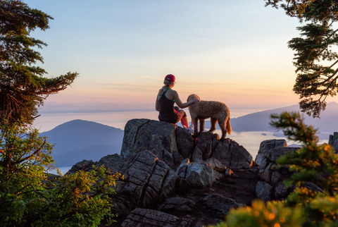 girl hiking with dog on rock with sunset view overlooking lake and mountains