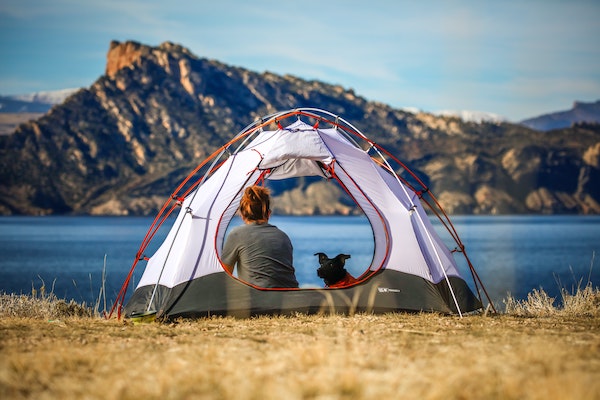 girl and dog sitting in tent looking at view of lake