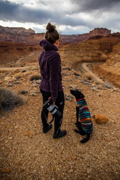 girl holding camera with dog in sweater hiking 