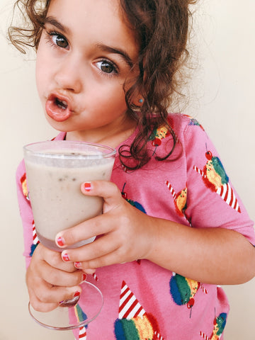 niña adorable usando camiseta rosada posando con un smoothie hecho en casa