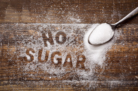 azúcar espolvoreada sobre mesa de madera con una cuchara de metal al lado con el texto "no sugar"