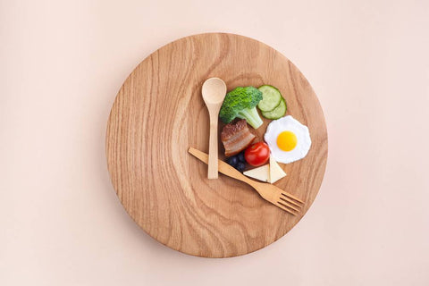 plato de madera decorado como reloj con cubiertos de madera y comida encima indicando horas de comer