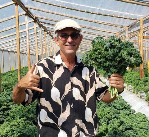 señor haciendo el "shaka sign" y sosteniendo hortalizas usando camisa con patrón de lirios