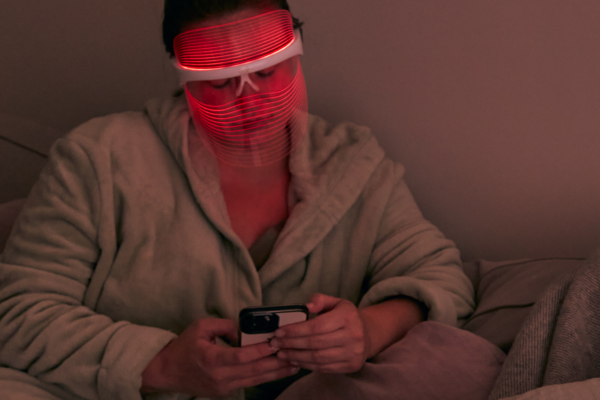 Model wearing MAGNITONE GetLit LED mask with red light on, while looking at her phone