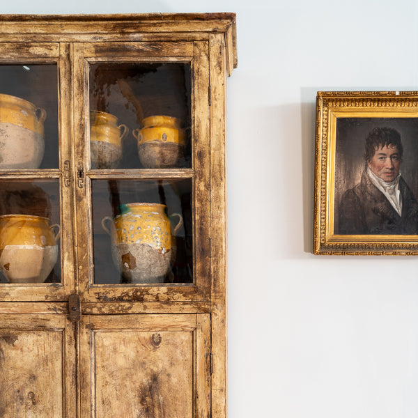 Antique French confit pots in bookcase vitrine with antique portrait painting